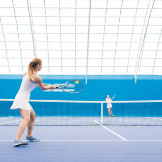 Wide angle portrait of young sportswoman hitting ball while playing tennis in court, copy space